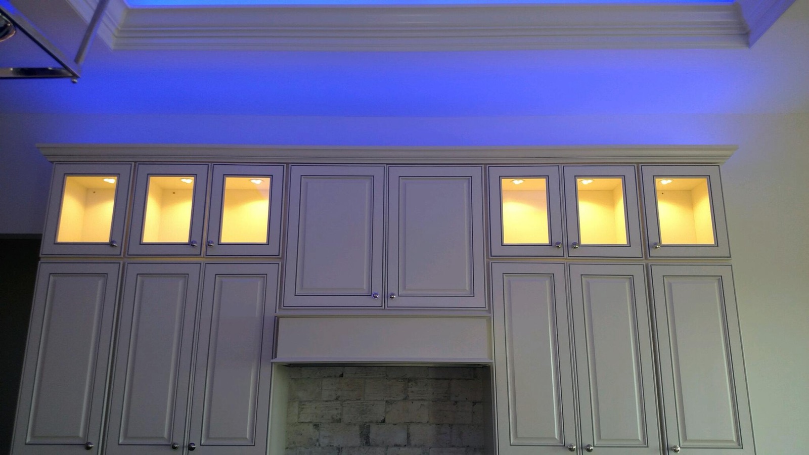 White kitchen cabinets with lit glass uppers and blue LED along the crown