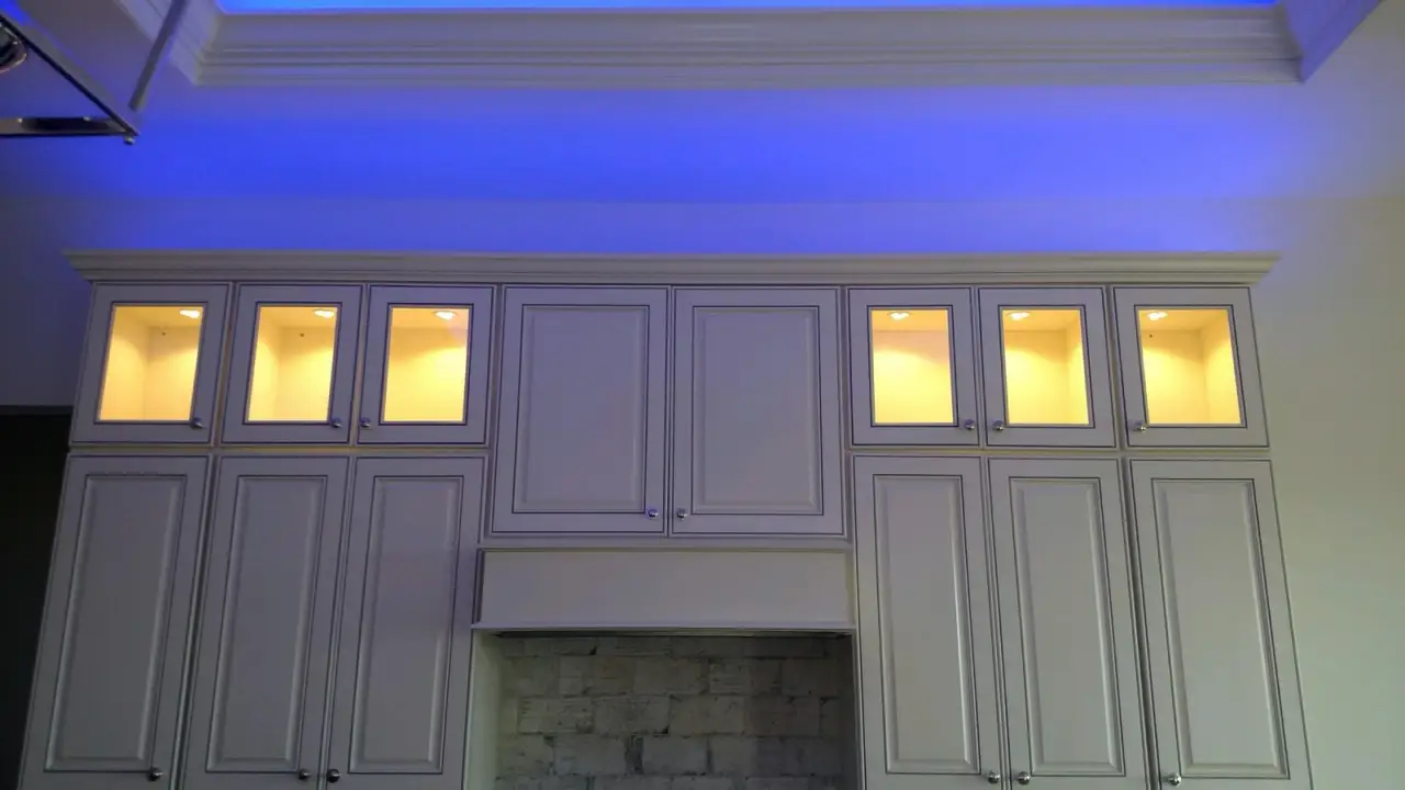 White kitchen cabinets with lit glass uppers and blue LED along the crown